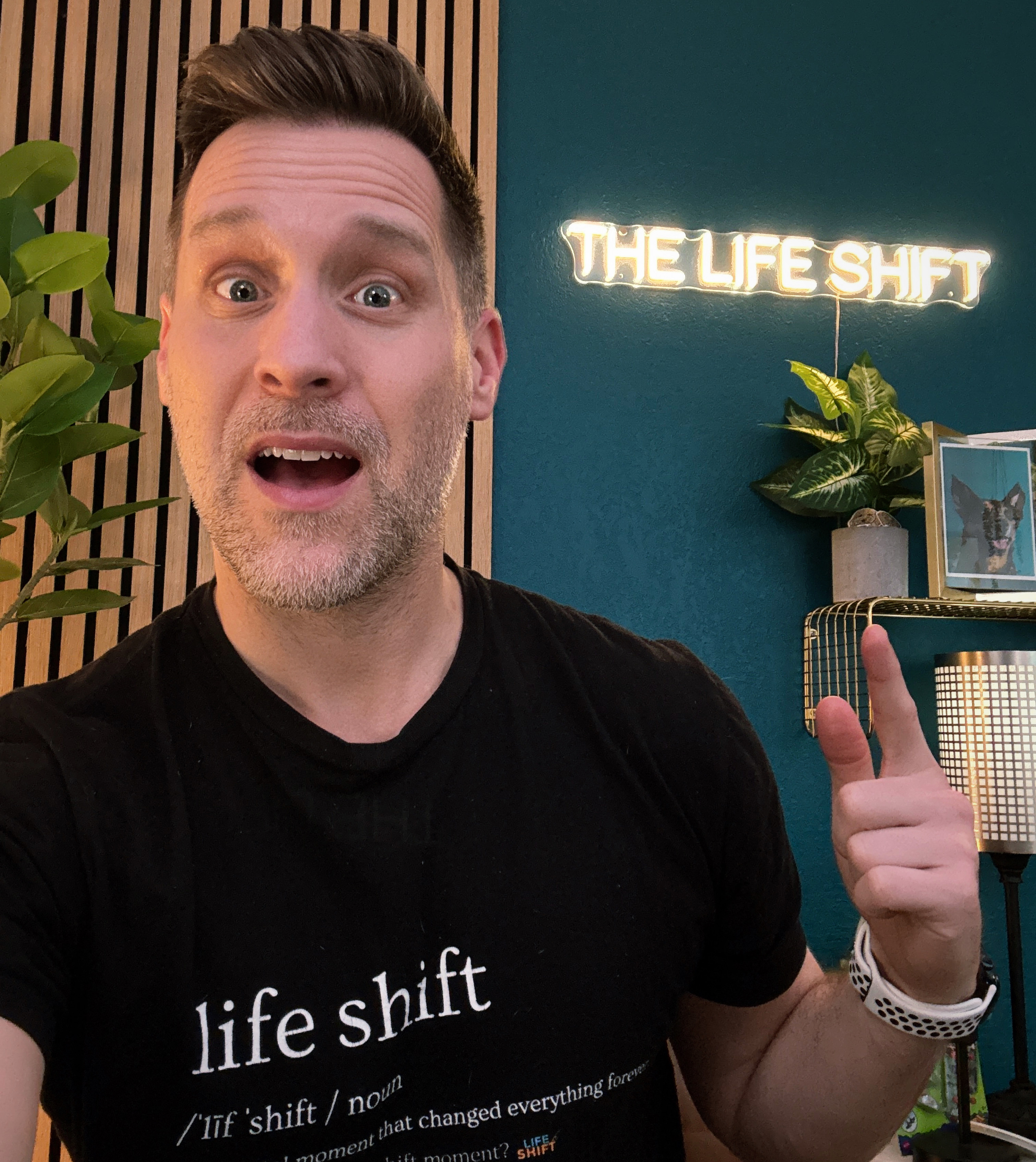 Matt Gilhooly, host of The Life Shift Podcast, in his home studio with The Life Shift neon sign